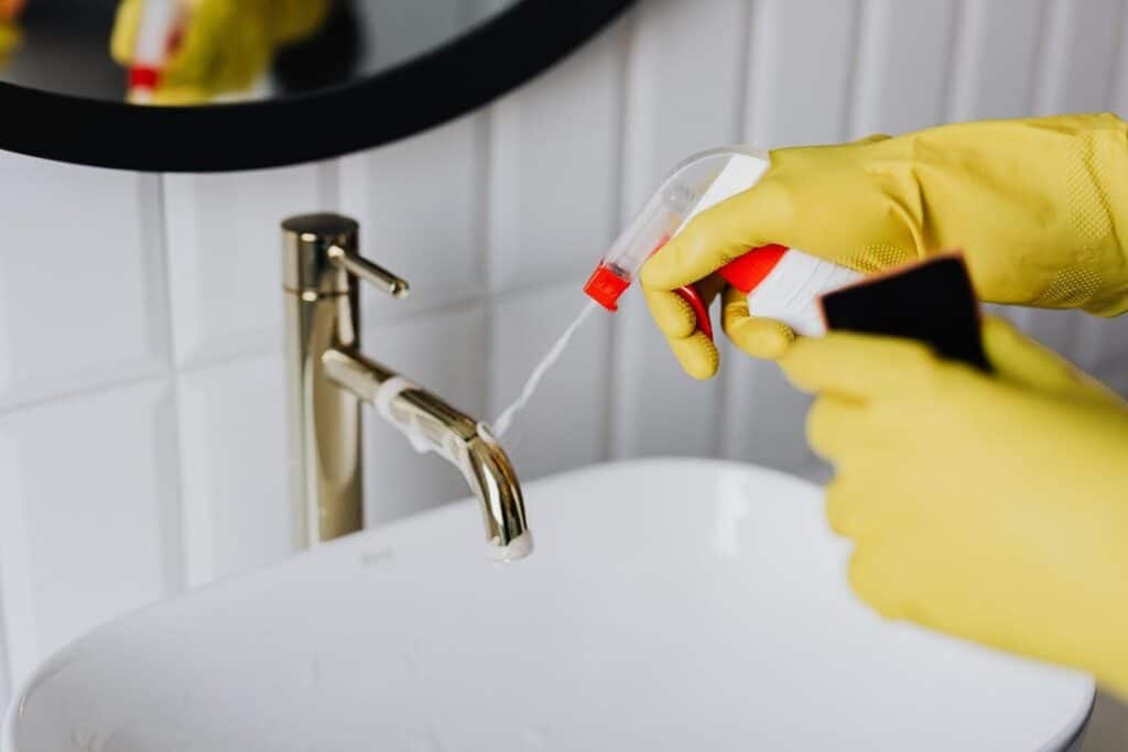 A cleaning specialist spraying disinfectant on bathroom tap