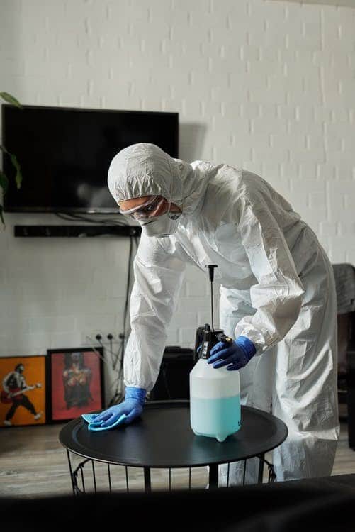 A cleaning specialist wearing PPE and disinfecting a table.